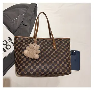 Detailed view of brown checkered tote bag with plush bear charm and leather handles