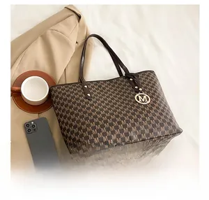 Detail view of large brown tote bag with all-over M-letter print and gold metal pendant