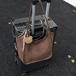 Minimalist large brown suede bucket bag with bear charm on black suitcase outdoors