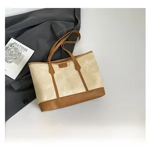 Detail of beige canvas tote bag with brown leather trim and long shoulder handles