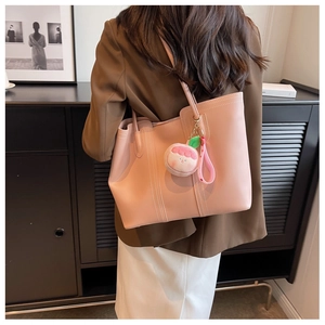 Pink faux leather tote bag with peach plush charm shown on a female model's shoulder