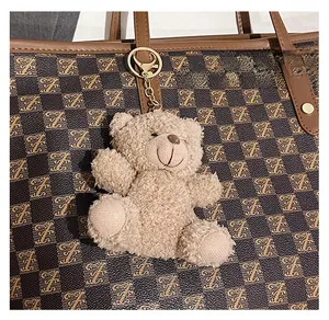 Close-up of a brown plush bear charm with gold keychain hanging on a tote bag