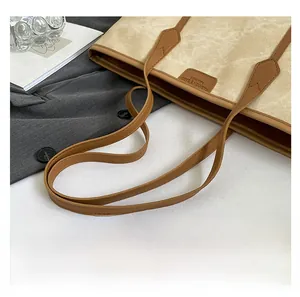Detail of beige canvas tote bag with brown leather handles and embossed fashion logo