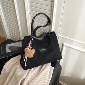 Large black corduroy tote bag with Creative Cat patch and plush bear charm on a seat