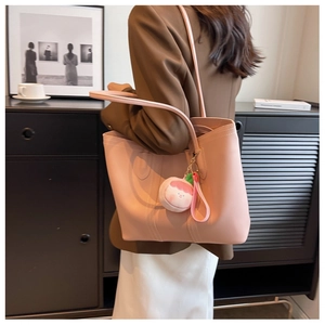 Close-up of a light pink leather tote bag with a peach plush charm and slim shoulder straps