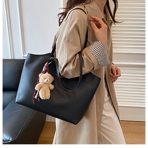Détail d'un sac cabas noir mat avec un pendentif ours en peluche et lettrage doré