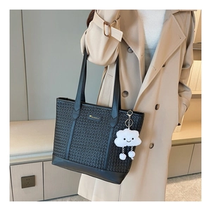 Détail d'un cabas noir tressé avec logo doré et pendentif nuage en peluche blanc doux