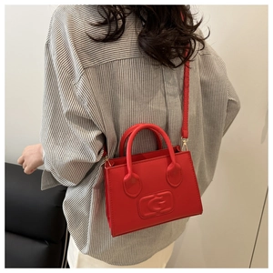 Detail of red leather crossbody bag with embossed logo worn by a model in casual outfit