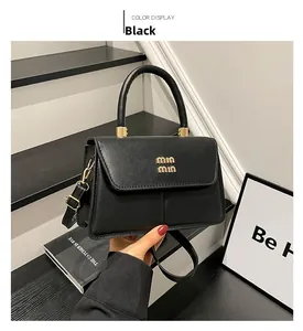 Detail of black faux leather handbag featuring gold min min lettering and curved handle