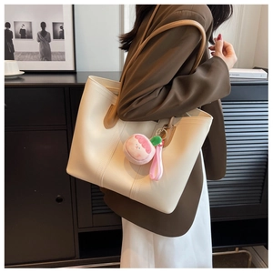 Minimalist beige tote bag with brown handles and a cute pink doll charm on the strap