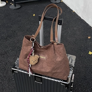 Brown quilted tote bag with large capacity and bear charm shown on a suitcase