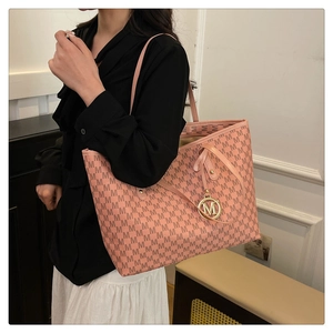 Detail of pink monogram tote bag with gold M-shaped charm and textured leather surface