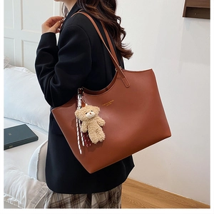 Détail d'un sac cabas en cuir marron avec charme ours en peluche et logo doré
