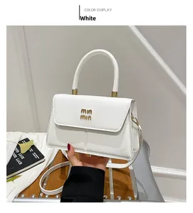 Detail shot of the white small square bag featuring a gold metal logo and sturdy top handle