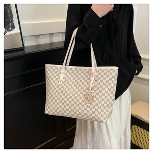 Close-up of beige leather tote bag with monogram print and golden metal pendant detail