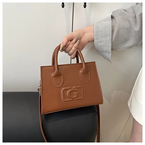 Detail shot of brown faux leather handbag featuring embossed G logo and dual handle straps