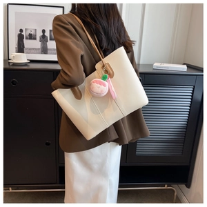 Detail of off-white leather tote bag with brown straps and peach plush charm on a model