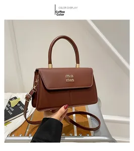 Close-up of brown crossbody bag with gold hardware and logo on a leather surface