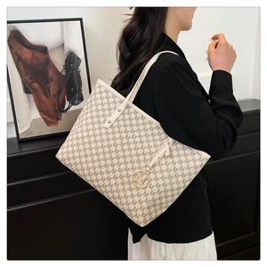 Detail of beige tote bag with M-pattern print and golden metal logo charm on shoulder