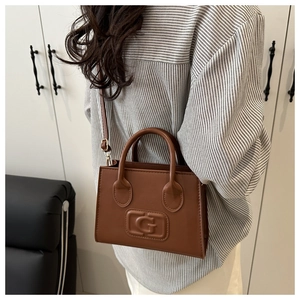 Detail of a brown leather tote bag featuring a prominent embossed G letter logo design
