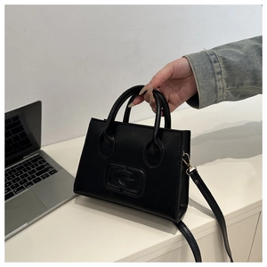 Detail of black crossbody bag with embossed G letter logo on a minimalist leather surface