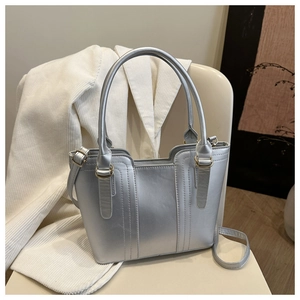 Close-up of metallic silver bucket bag with decorative stitching on a cream-colored chair
