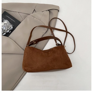 Detail einer braunen Wildleder-Schultertasche mit Doppelriemen auf beige Sakko