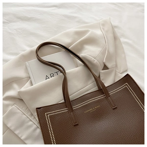 Détail du cabas en cuir marron foncé avec lettrage doré et surpiqûres blanches élégantes