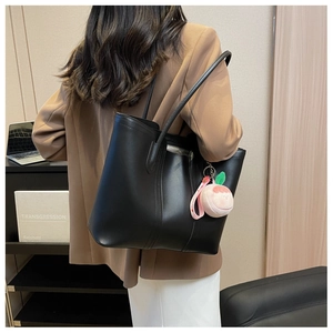 Detailed view of black large capacity tote bag with a pink peach plush charm on a model