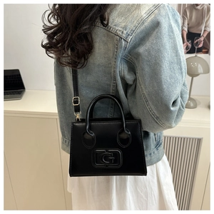 Detail of a black leather crossbody bag with embossed G logo shown on model with denim jacket