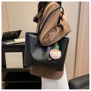 Side view of large black tote bag with cute pink doll charm on a female shoulder