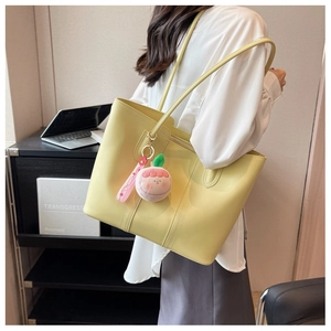 Detail of pale yellow tote bag with dual straps and cute pink peach charm accessory