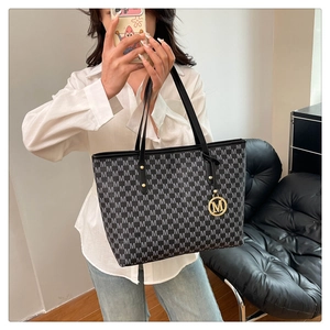 Detail of black monogram tote bag with gold metal logo charm and leather texture