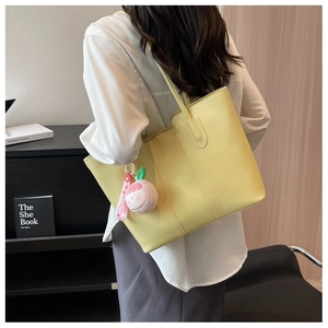 Detail of stylish bright yellow leather tote bag with a cute pink peach plush charm