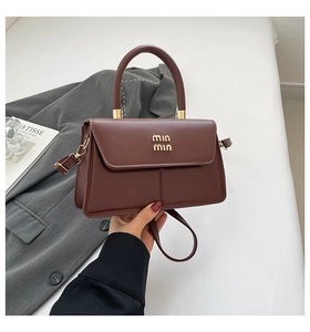 Detail of chocolate brown leather crossbody bag with gold logo and round handle