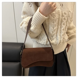 Brown suede underarm bag styled with a white knit sweater in a cozy indoor setting