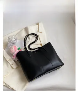 Detail of black matte leather tote bag with slim handles and cute peach bag charm