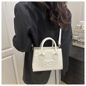 Close-up of white mini square bag with embossed G design on a black blazer model