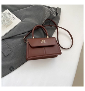 Detail of a dark brown leather mini bag with gold hardware on a grey blazer suit