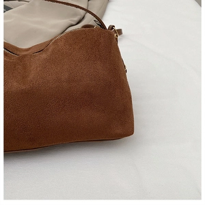 Detailansicht der braunen Wildlederstruktur und des goldenen Reißverschlusses der Tasche