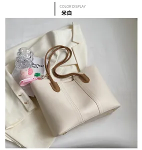 Detail of off-white tote bag featuring brown straps, gold bottom studs, and peach charm