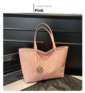 Pink tote bag detail with all-over M letter print and gold logo charm on black desk
