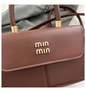 Detail of dark brown leather handbag featuring golden logo and fine grain texture