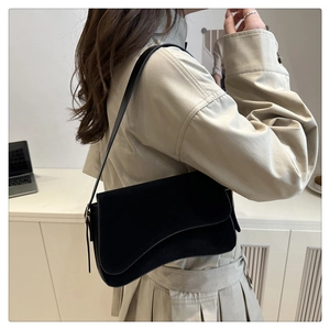 Minimalist black baguette bag with asymmetric flap shown in a modern office setting
