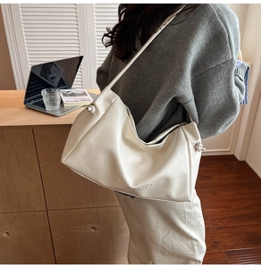 Detail of minimalist cream-colored shoulder bag with embossed letters and knot straps