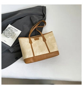 Top-down view of a beige canvas tote bag with brown leather trim on a grey blazer