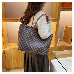 Detail of checkered tote bag with brown straps and gold rivets on a wooden display
