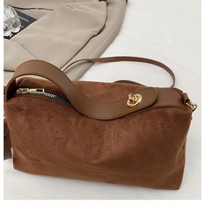 Makroaufnahme einer braunen Wildledertasche mit goldenen Beschlägen und glattem Lederbesatz
