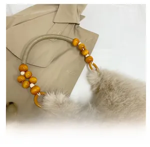 Detail of faux rabbit fur handbag featuring wooden and white beaded handle on trench coat