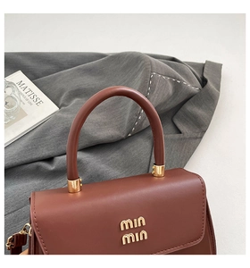 Close-up of brown leather handbag with gold logo and cylindrical metal hardware